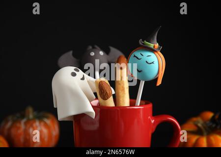 Verschiedene Tortenknöpfe im Becher, dekoriert als Monster, Nahaufnahme. Halloween-Leckerbissen Stockfoto