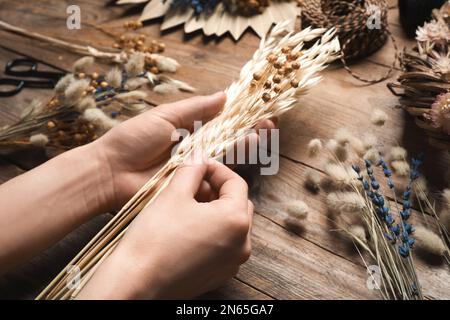 Florist, der einen Blumenstrauß aus getrockneten Blumen auf einem Holztisch macht, Nahaufnahme Stockfoto
