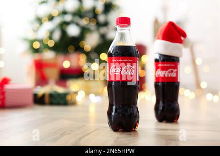 MYKOLAIV, UKRAINE - 01. Januar 2021: Flaschen Coca-Cola auf dem Boden vor verschwommenen Weihnachtslichtern Stockfoto