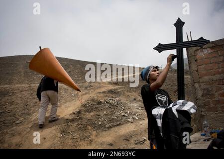 A musician makes his way up a hill path hauling his harp, as a young man adds a fresh coat of paint on the cross of a relative's grave in the Nueva Esperanza cemetery during the Day of the Dead celebrations in Lima, Peru, Friday, Nov. 1, 2013. The souls of departed loved ones are being honored around Latin America as celebrants blend pre-Columbian rituals with the Roman Catholic observance of all Saint’s Day on Nov. 1 and All Soul’s Day on Nov. 2 to mark the Day of the Dead. (AP Photo/Rodrigo Abd)