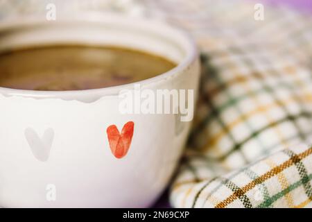 Weißer, handbemalter Keramikbecher mit Liebessymbolen. Rote graue Herzen auf einer Tasse. Heißer Kaffee, Cappuccino-Kakao, Espresso, heißes Schokoladengetränk. Co Stockfoto