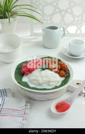 Servieren einer Schüssel mit süßem Haferbrei und Stärkebällen mit brauner Zuckersauce und Kokosmilch Stockfoto