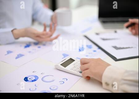 Zugeschnittenes Bild einer Buchhalterin mit Taschenrechner, Berechnung und Analyse von Finanzdaten, die mit ihren Kollegen an einem Bericht arbeitet. Stockfoto