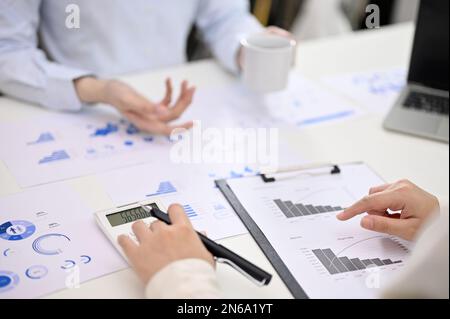 Zugeschnittenes Bild einer Buchhalterin mit Taschenrechner, Berechnung und Analyse von Finanzdaten, die mit ihren Kollegen an einem Bericht arbeitet. Geschäftskonsolidierung Stockfoto
