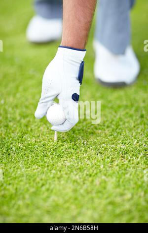 Zum Abschlag. Ein männlicher Golfer, der einen weißen Golfen trägt und seinen Golfball und sein T-Shirt in den Boden legt. Stockfoto