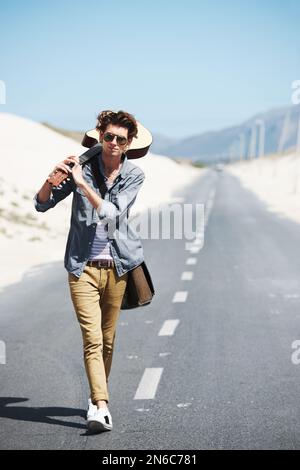 Ich muss zu diesem Gig. Trendiger junger Mann, der seine Gitarre über die Schulter hält, wenn er die Straße hinuntergeht. Stockfoto