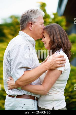 Es ist ein Zeichen wahrer Liebe. Ein liebevoller älterer Mann, der seine Frau auf die Stirn küsst. Stockfoto