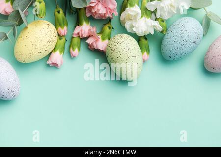 Osterfarbene Eier und ein Strauß weißer und rosafarbener Nelken mit Eukalyptuszweigen auf einem weichen grünen Hintergrund. Festlicher Hintergrund. Stockfoto