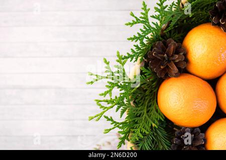 Tangerinen in einem Korb nah - auf einem grauen Holztisch neben den Nadelzweigen von Wacholderbeeren und Zapfen. Hintergrund zu Weihnachten. Winterurlaub. Flach Stockfoto