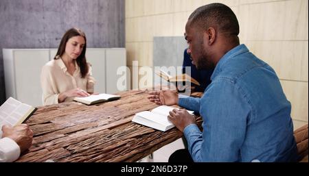 Junge, Multiethnische Menschen, Die Über Dem Holzschreibtisch Bibel Lesen Stockfoto