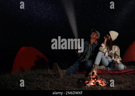 Glückliches Paar mit Taschenlampe nahe Lagerfeuer in der Nacht. Campingsaison Stockfoto