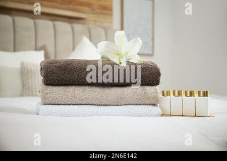 Stapel sauberer Handtücher, Blumen- und Shampooflaschen auf dem Bett im Haus Stockfoto
