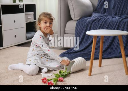 Emotionales kleines Mädchen und zerbrochene Keramikvase auf dem Boden zu Hause Stockfoto