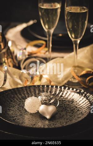 Tischdekoration mit dekorativem Herzen, zwei Gläser mit Sekt- und Partydekoration, Schwarz und Gold, vertikal Stockfoto