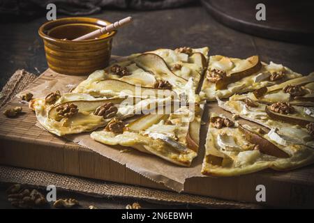Flammentorte mit Birne, Ziegenkäse, Honig und Walnüssen auf dunklem rustikalem Holzhintergrund Stockfoto