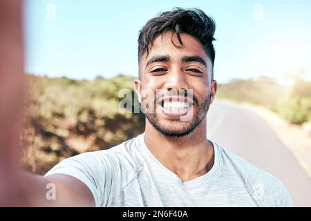 Ein Mann aus dem Mischrennsport macht beim Laufen ein Selfie. Attraktiver hispanischer männlicher Athlet, der während des Trainings lächelt, um ein Selbstporträtfoto zu machen Stockfoto