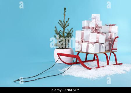 Schlitten mit Geschenkboxen und kleiner Tanne auf hellblauem Hintergrund. Platz für Text Stockfoto