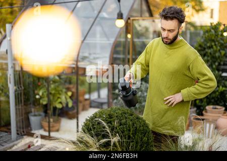 Guy schneidet einen runden Busch mit einer Schere Stockfoto