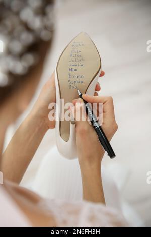 Die junge Braut schreibt die Namen ihrer Single-Freunde drinnen auf Schuhe, Nahaufnahme. Hochzeitsabergläubisch Stockfoto