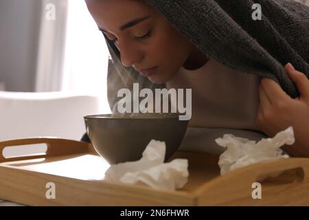 Eine Frau mit Karomuster, die drinnen über der Schüssel inhaliert Stockfoto