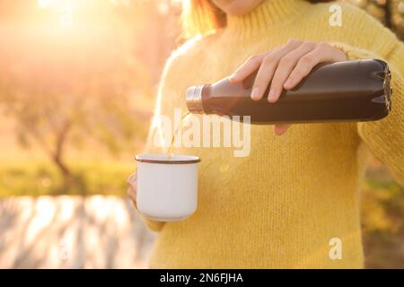 Frau, die draußen ein heißes Getränk aus der Thermosflasche in den Becher gießt, Nahaufnahme Stockfoto