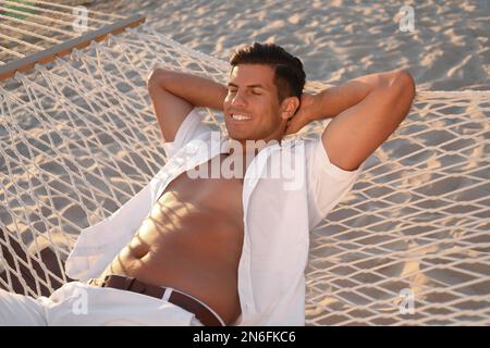 Ein Mann, der sich bei Sonnenuntergang in einer Hängematte am Strand entspannt Stockfoto