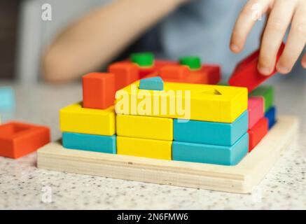 Nahaufnahme von Kinderhänden, die mit einem pädagogischen, mehrfarbigen Puzzle aus umweltfreundlichem Holzmaterial spielen Stockfoto