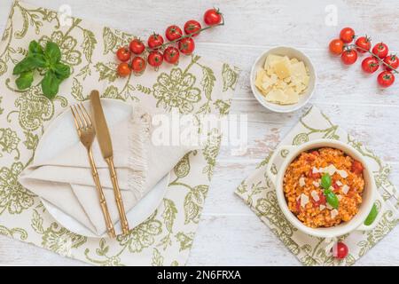 Tischdecken mit frischem Tomaten-Risotto mit Basilikum und Parmesan, Draufsicht Stockfoto