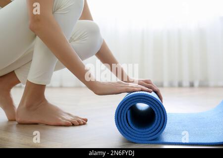 Frau rollt blaue Yoga-Matte drinnen, Nahaufnahme Stockfoto