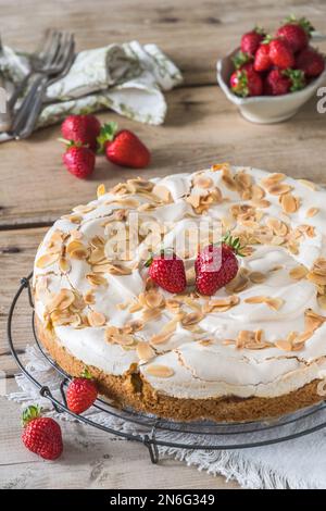 Ganze Rhabarberkuchen mit Baiser-Belag, geröstete Mandeln und frische Erdbeeren auf einem Kühlregal auf einem alten rustikalen Holztisch, vertikal Stockfoto