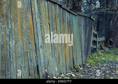 Nahaufnahme eines wackeligen Holzzauns mit Herbstlaub auf dem Boden Konzeptfoto Stockfoto