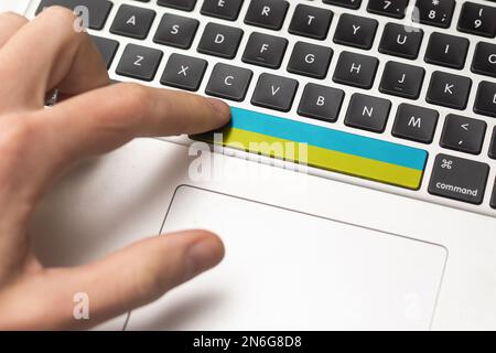 Durch Drücken der Eingabetaste mit ukrainischer Flagge wird ein Cyberangriff auf die Ukraine dargestellt, eine Metapher des Erlernens ukrainischer Sprache, schwarze Tastatur, Nahaufnahme, Vorderseite Stockfoto