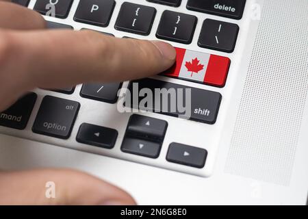 Computerschlüssel mit dem Kanada drauf. Männliche Hand drückt Computertaste mit kanadischer Flagge. Stockfoto