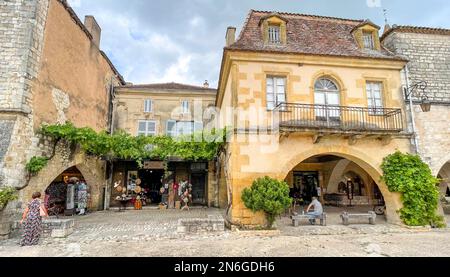 Alte, mit Weinblättern bedeckte Häuser mit typischen Souvenirläden auf dem Marktplatz in der historischen Altstadt von Monpazier, Departement Dordogne Stockfoto