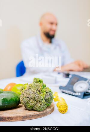 Konzentrieren Sie sich auf Gemüse von Ernährungsexperten mit Laptop am Schreibtisch. Ernährungswissenschaftler, der an einem Laptop arbeitet, der Kunden in der Klinik online berät, konzentrieren sich auf Stockfoto