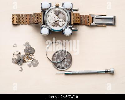 Draufsicht auf offene Armbanduhr mit rostigem Armband auf Holztisch in Uhrmacherwerkstatt Stockfoto