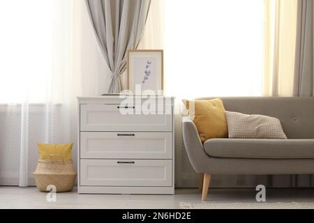 Sofa und Kommode in der Nähe des Fensters mit stilvollen Vorhängen im Wohnzimmer. Innendesign Stockfoto