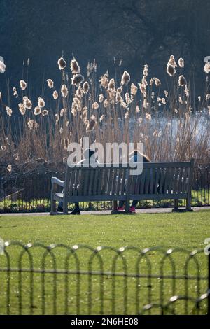 London, England, Großbritannien. Zwei Frauen, die im Februar auf einer Bank im St. James's Park sitzen Stockfoto