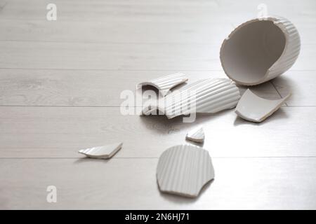 Zerbrochene weiße Keramikvase auf Holzboden Stockfoto