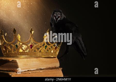 Fantasiewelt. Schwarze Krähe, beleuchtet von magischem Licht, das auf der goldenen Krone sitzt Stockfoto
