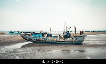Ein traditionelles hölzernes Fischerboot liegt bei Ebbe am Strand von Tra Co, an der Grenze zu China nahe Mong Cai, Vietnam. Stockfoto