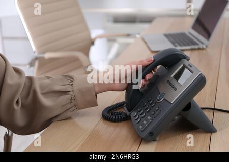 Frau, die Tischtelefon am Holztisch im Büro benutzt, Nahaufnahme. Hotline-Service Stockfoto