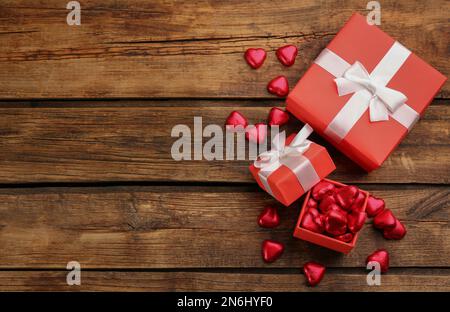 Herzförmige Schokoladenbonbons und Geschenkschachteln auf Holztisch, flach liegend. Platz für Text Stockfoto