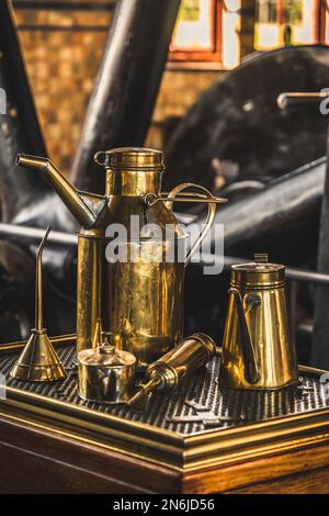 Alte Messing-Ölkannen für Schmiermaschinen. Turbine einer Dampfmaschine im Hintergrund. Konzentrieren Sie sich auf den großen Ölkanister. Übersetzung des Textes "Lichte Machi Stockfoto