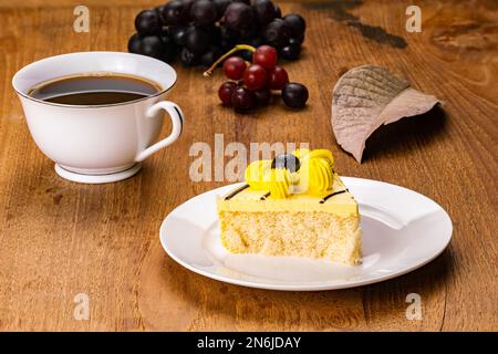 Frühstück mit hausgemachtem, köstlichem Kuchen mit gelber Blumencreme in weißer Keramikschale mit einer Tasse schwarzem Kaffee und Bündeln reifem Gummi Stockfoto