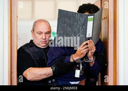 Frankenthal, Deutschland. 10. Februar 2023. Der Beklagte (r) wird von einem Gerichtsbediensteten in den Anhörungssaal des Landesgerichts geführt. Etwa vier Monate nach dem Messerangriff, bei dem zwei Tote und einer schwer verletzt wurden, in Ludwigshafen-Oggersheim in Rheinland-Pfalz beginnt der Prozess gegen den mutmaßlichen Täter, einen 26-jährigen Mann aus Somalia. Der Angeklagte soll am 18. Oktober 2022 einen 20-Jährigen und einen 35-Jährigen mit einem Küchenmesser auf der Straße getötet haben. Kredit: Uwe Anspach/dpa/Alamy Live News Stockfoto