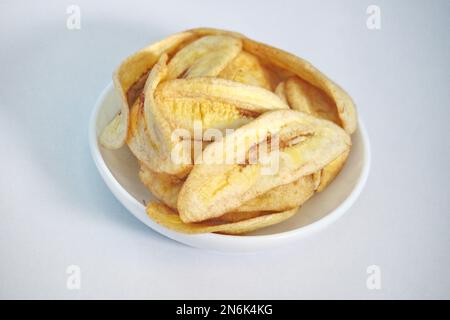 Eine Nahaufnahme von getrockneten Bananenchips in einer weißen Schüssel, isoliert auf einem hellen Hintergrund Stockfoto