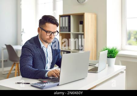 Konzentrierter Executive Manager, der Finanzmarktforschung betreibt, während er im Büro an einem Notebook arbeitet. Stockfoto