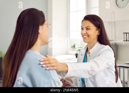 Eine freundliche, lächelnde Ärztin, die die Schulter der Frau hält und ihr positive Nachrichten über ihre Gesundheit mitteilt. Stockfoto