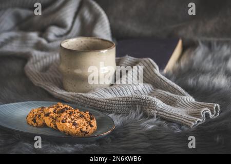 Schokoladenkekse und eine Tasse mit grauem Fell und Wollpullover, gemütliche Winterkaffeeszene Stockfoto